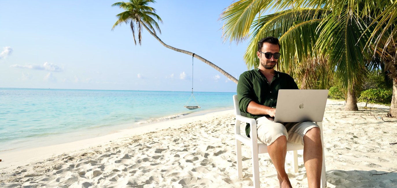 An engineer working on a laptop from a beach, monitoring a lighting system remotely