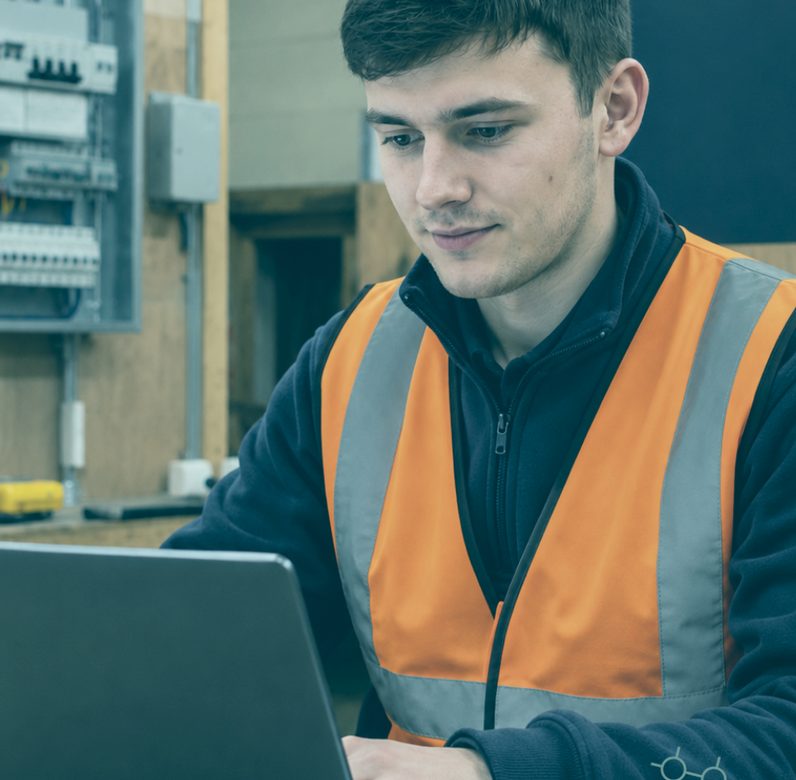 Technician working on a laptop beside an electrical switchboard